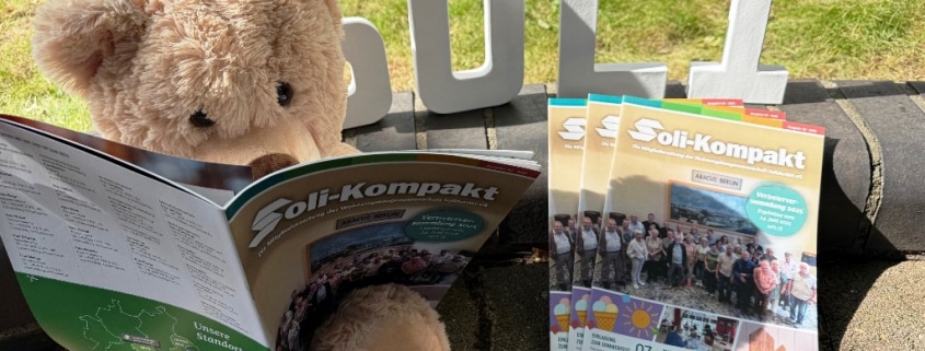 Soli-Bär sitzt draußen und blättert in der neuen Mitgliederzeitung der Wohnungsbaugenossenschaft Solidarität eG, daneben liegen 3 Ausgaben der Zeitung. Im Hintergrund sind die Buchstaben S, O, L, I zu sehen.