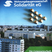 Stadtbild mit Mehrfamilienhäusern, Im Vordergrund ein Objekt der Wohnungsbaugenossenschaft Solidarität eG, darauf stehen kleine menschliche Holzfiguren