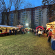 Weihnachtsmarktstände auf einer Rasenfläche, Karussell, Bühne und im Hintergrund ein großes Wohnhaus.