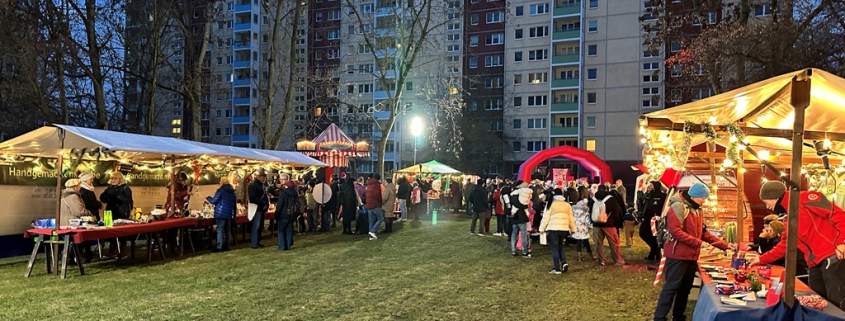 Weihnachtsmarktstände auf einer Rasenfläche, Karussell, Bühne und im Hintergrund ein großes Wohnhaus.