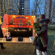 WG Solidarität Mann hält Kind auf dem Arm und wirft mit einem Ball auf gestapelte Büchsen.