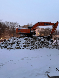 Ein H&uuml;gel aus Schutt mit einem Bagger oben drauf. Alles ist mit einer Schneedecke &uuml;berzogen.