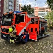 Feuerwehrauto Ein Feuerwehreinsatzwagen steht mit geöffneten Türen und sichtbarer Einsatzkleidung vor einem Wohnhaus