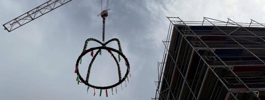 Richtkranz wird mittels eines Krahns auf den Neubau eines Mehrfamilienhauses gehoben