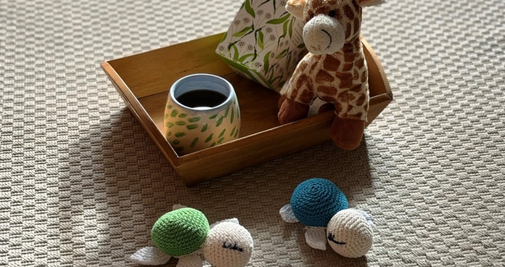 Tablett mit einer Tasse Tee dekoriert mit einer kleinen Kuscheltiergiraffe. Davor liegen zwei kleine geh&auml;kelten Schildkr&ouml;ten.