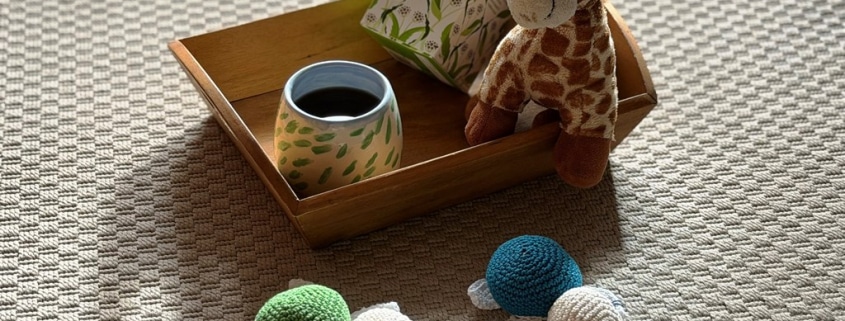 Tablett mit einer Tasse Tee dekoriert mit einer kleinen Kuscheltiergiraffe. Davor liegen zwei kleine gehäkelten Schildkröten.
